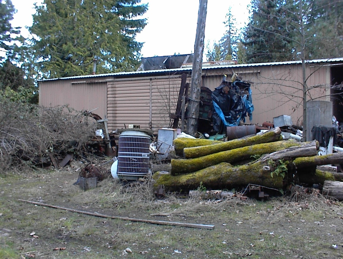 Shed exterior with moss-covered logs and old machinery