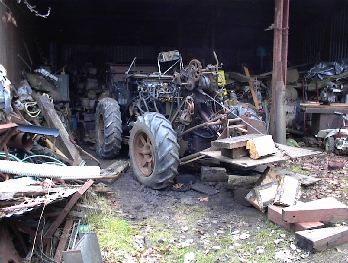 Vintage tractor stripped down in cluttered shed with farm equipment