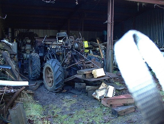 Vintage tractor in shed viewed from side with debris on ground