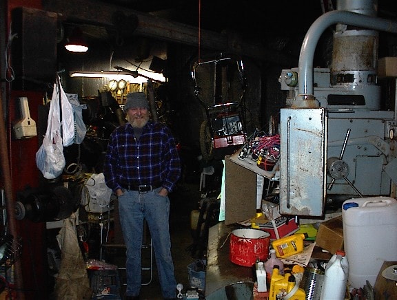 Man standing in shed doorway surrounded by tools and workshop equipment