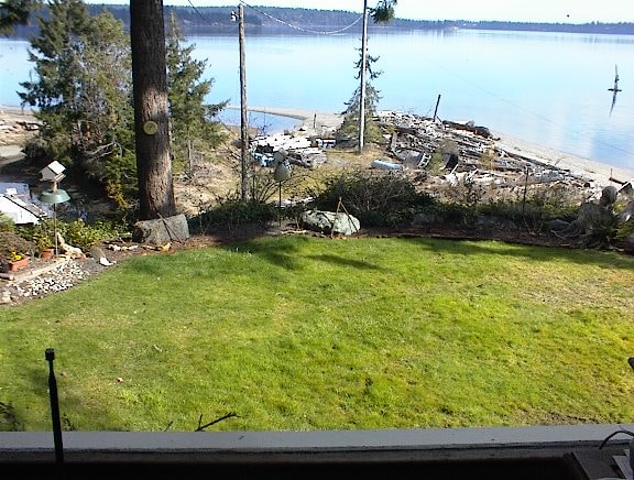 Yard and beach with boathouse debris on the shoreline and calm bay beyond