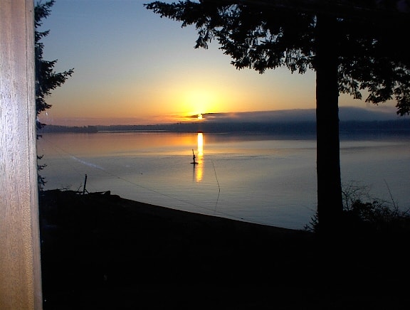 Second sunrise photo over still water with silhouetted trees and buoy