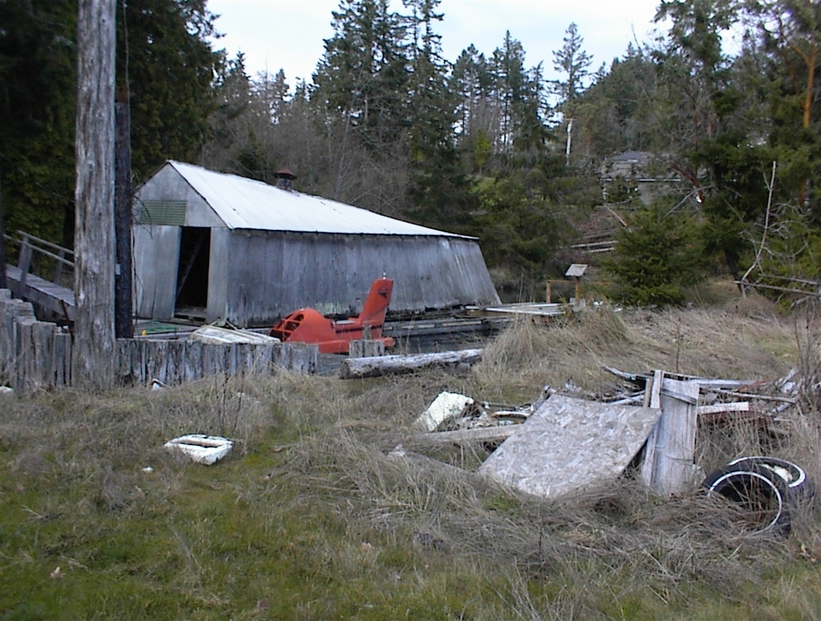 Old boathouse shed with red equipment and debris in the yard
