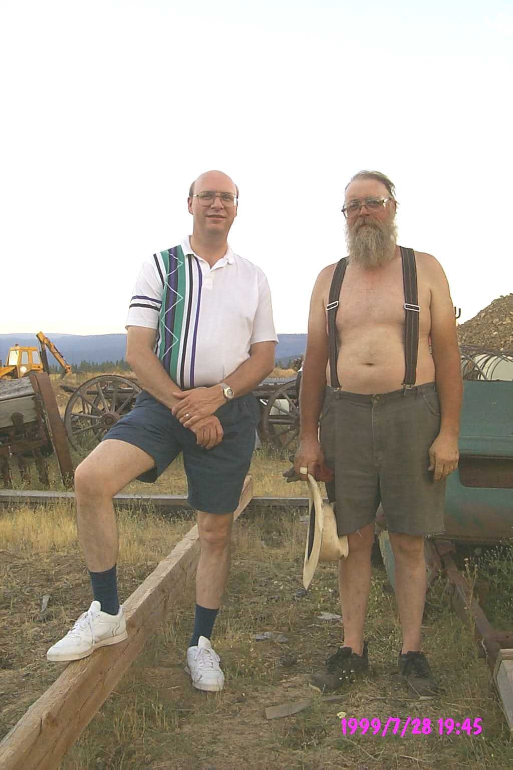 Randy and Joe posing together outdoors with farm equipment in the background