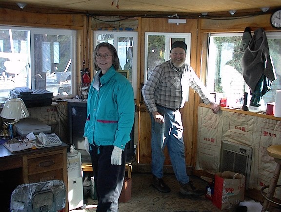 Two people inside the houseboat pilothouse with water visible through the windows